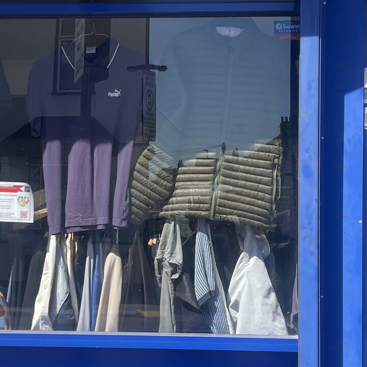 A navy polo shirt and a quilted olive gilet above a rail of folded shirts
